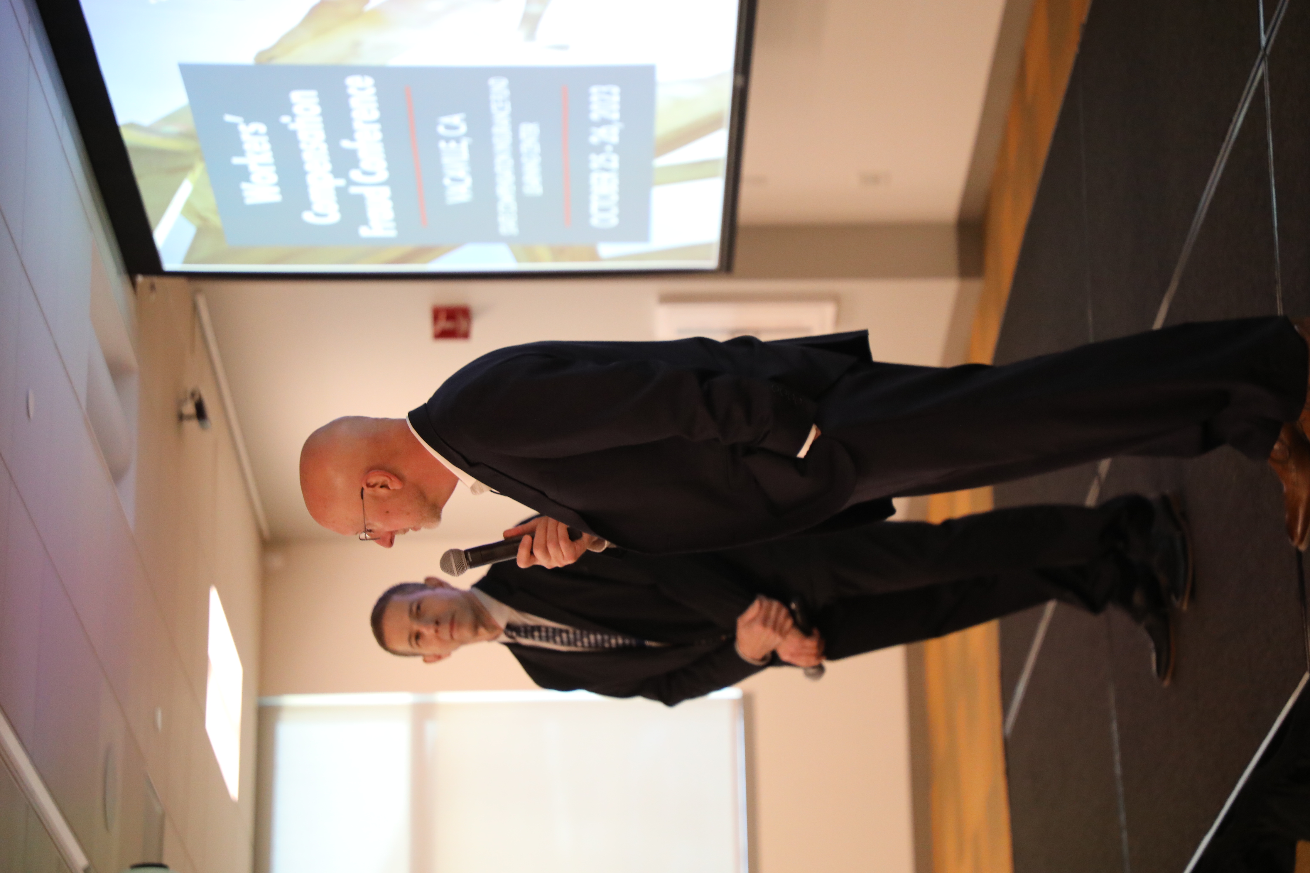 Two older light-skinned male-presenting speakers present at a workers' compensation conference.