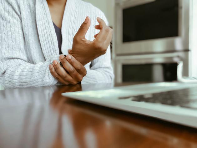 A closeup of a person sitting at a desk clutching their hand.